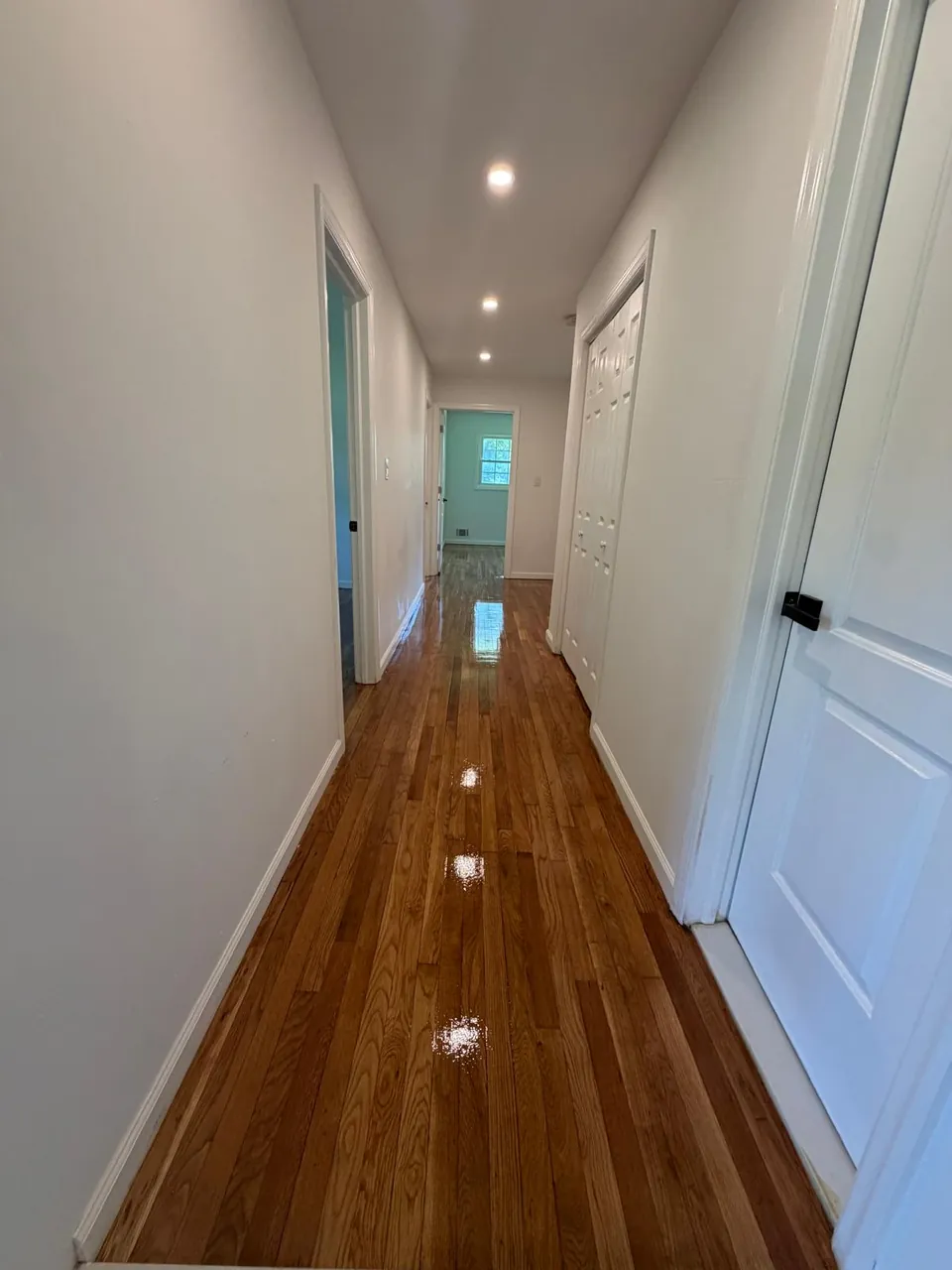 Long hallway with a glossy refinished oak floor and white doors